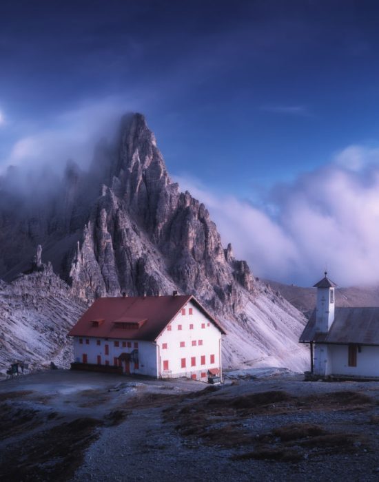 House and church sit on a hillside in Italy with fog-covered mountains just beyond